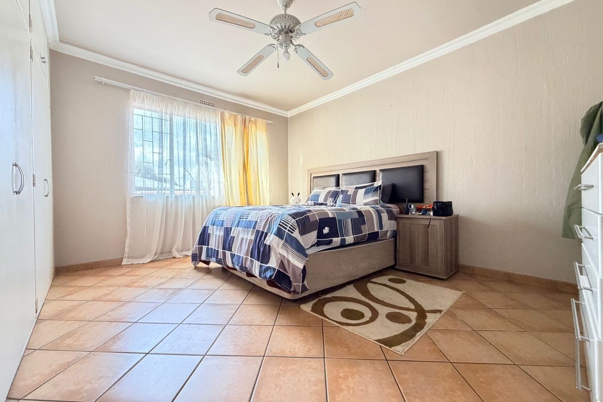 A spacious bedroom featuring tiled flooring, built-in cupboards, and a ceiling fan, offering a functional and well-maintained living space.