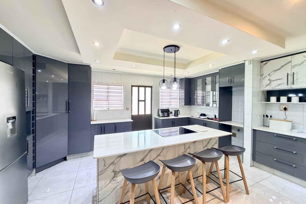 Modern, high-end kitchen featuring sleek grey cabinetry, a marble-topped central island with integrated hob, and sophisticated recessed ceiling lighting.