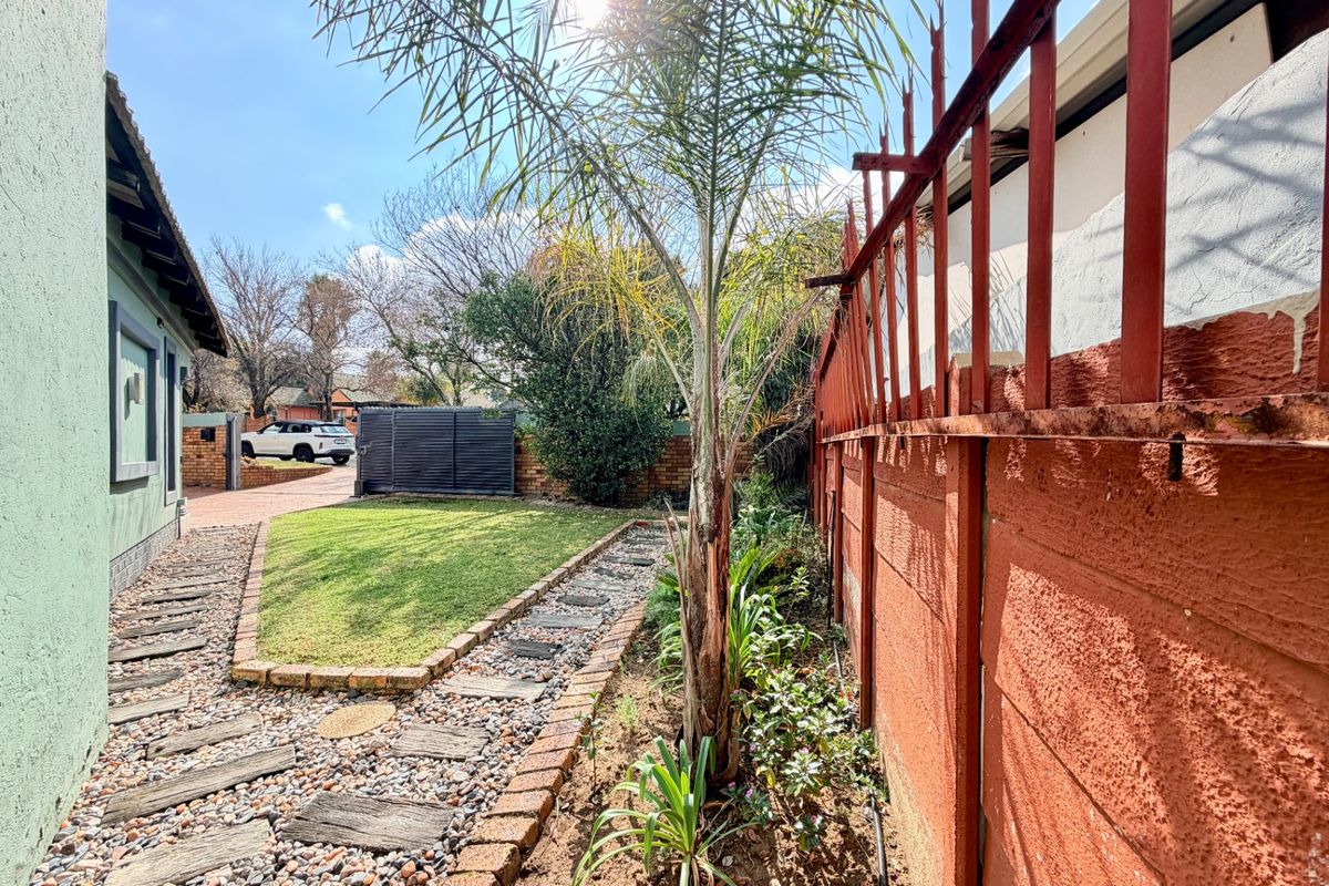 A side garden area featuring a paved walkway, lawn, and a precast concrete boundary wall with metal security spikes.