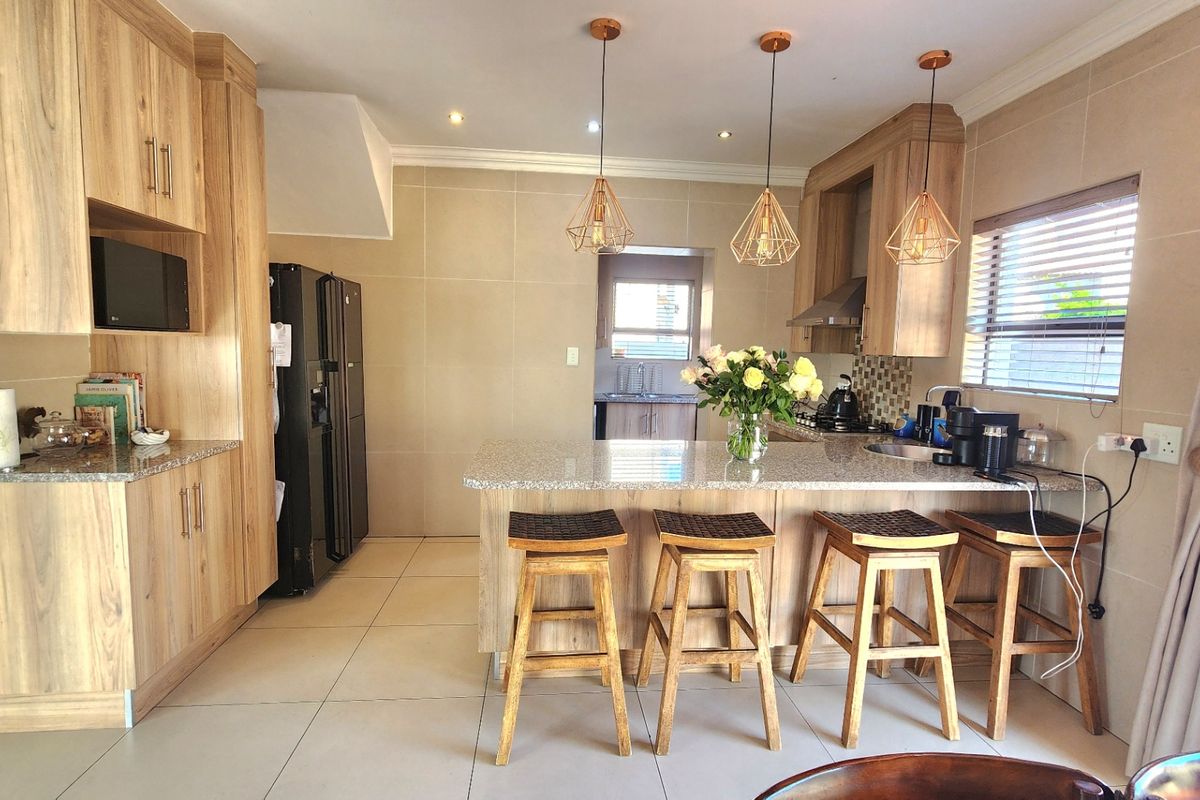 Modern kitchen featuring wood-finish cabinetry, granite countertops, a central island with breakfast bar seating, and contemporary pendant lighting.