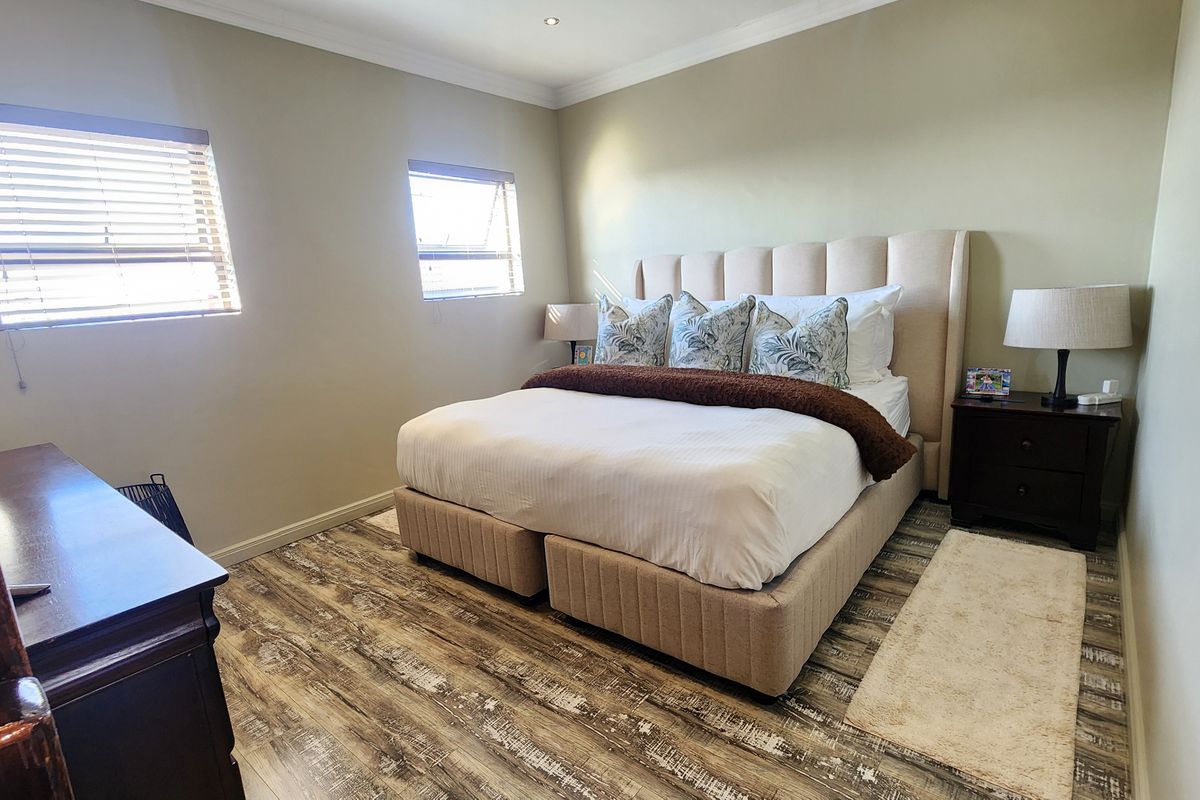 A well-maintained bedroom featuring durable laminate flooring, recessed downlighting, and neutral wall finishes with fitted window blinds.