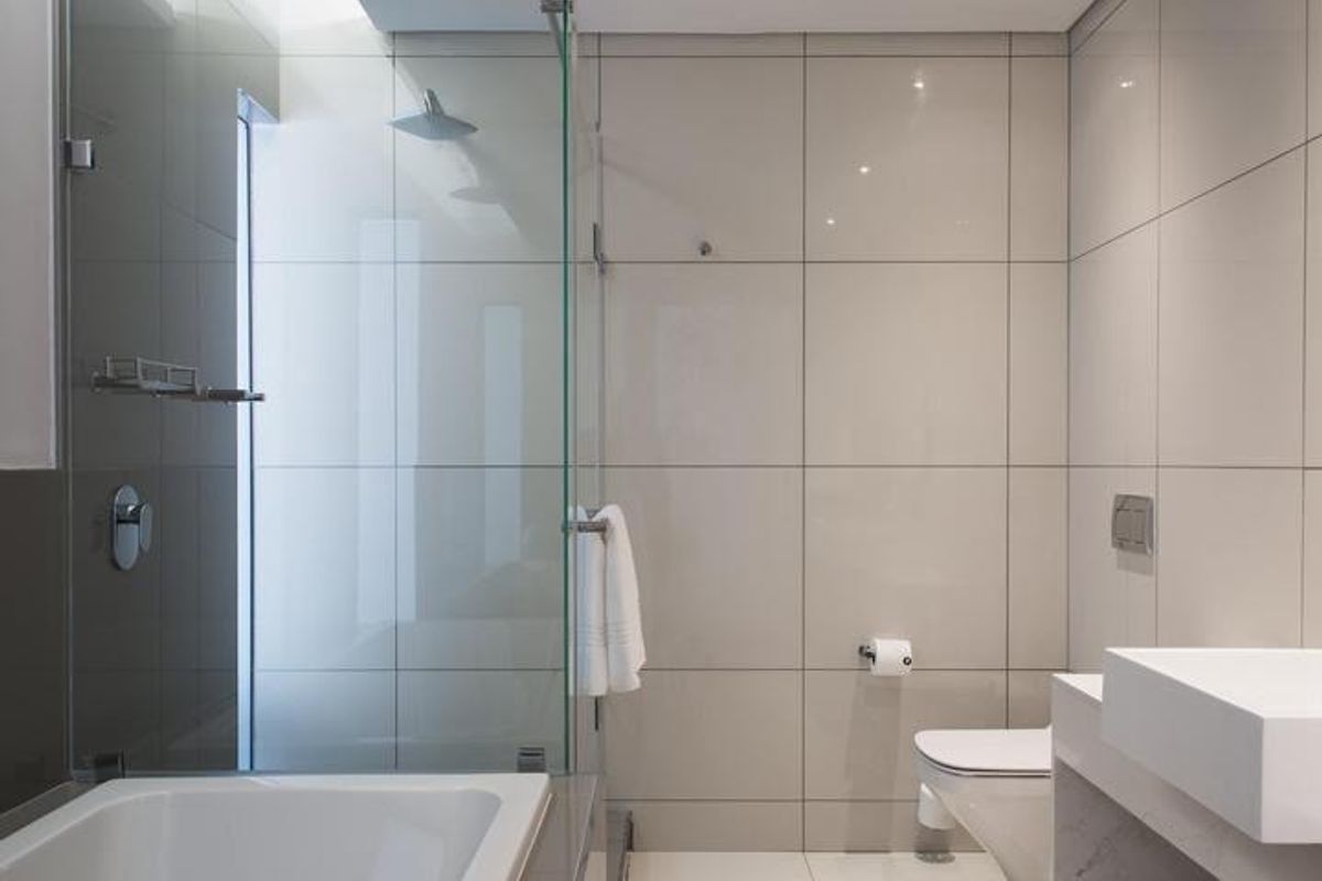 Modern bathroom featuring a glass-enclosed rain shower, built-in bathtub, wall-mounted toilet, and a sleek floating vanity with high-quality tiled finishes.
