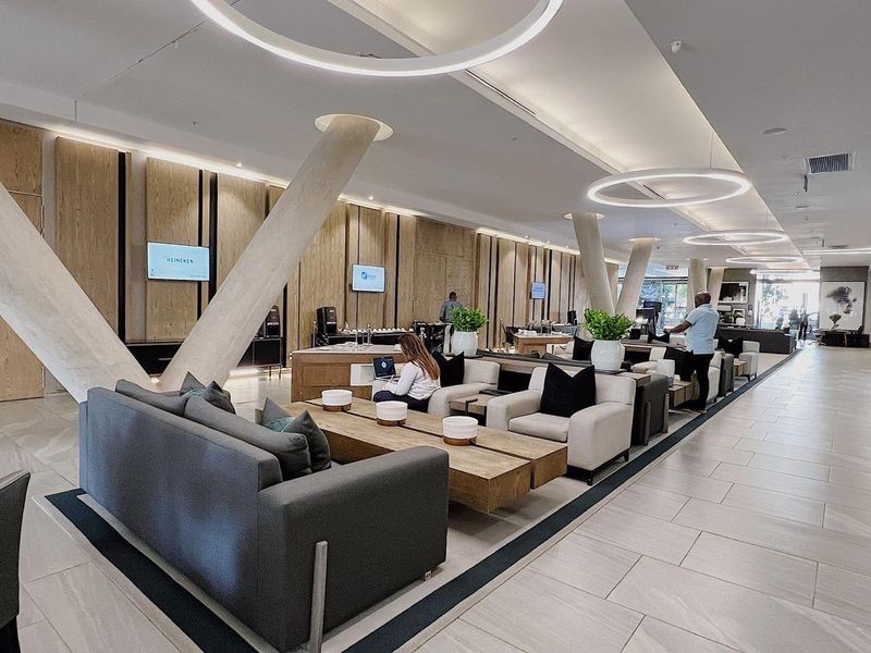 Modern, spacious clubhouse lounge featuring high-end timber wall paneling, contemporary circular pendant lighting, and large-format tiled flooring in a well-maintained communal area.