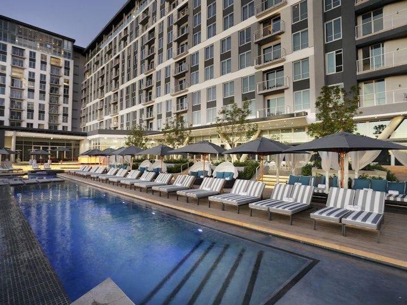 A well-maintained swimming pool area featuring timber decking and modern apartment building architecture in the background.