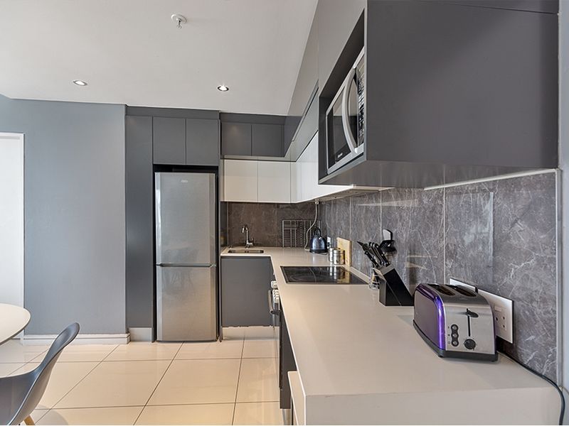 Modern kitchen featuring sleek grey and white cabinetry, stone countertops, integrated microwave, electric hob, and stylish tiled splashback in a contemporary apartment setting.