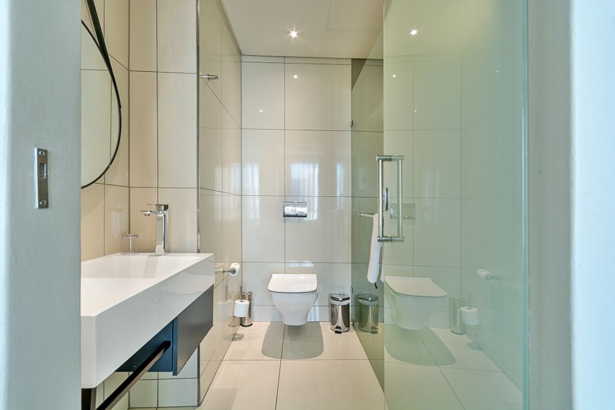 Modern bathroom featuring a wall-mounted toilet, glass shower enclosure, and a sleek vanity basin with contemporary chrome fixtures and neutral tiling.