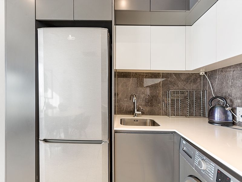 Modern kitchen area featuring sleek grey and white cabinetry, stone countertops, integrated laundry appliance, and a stylish stone splashback.