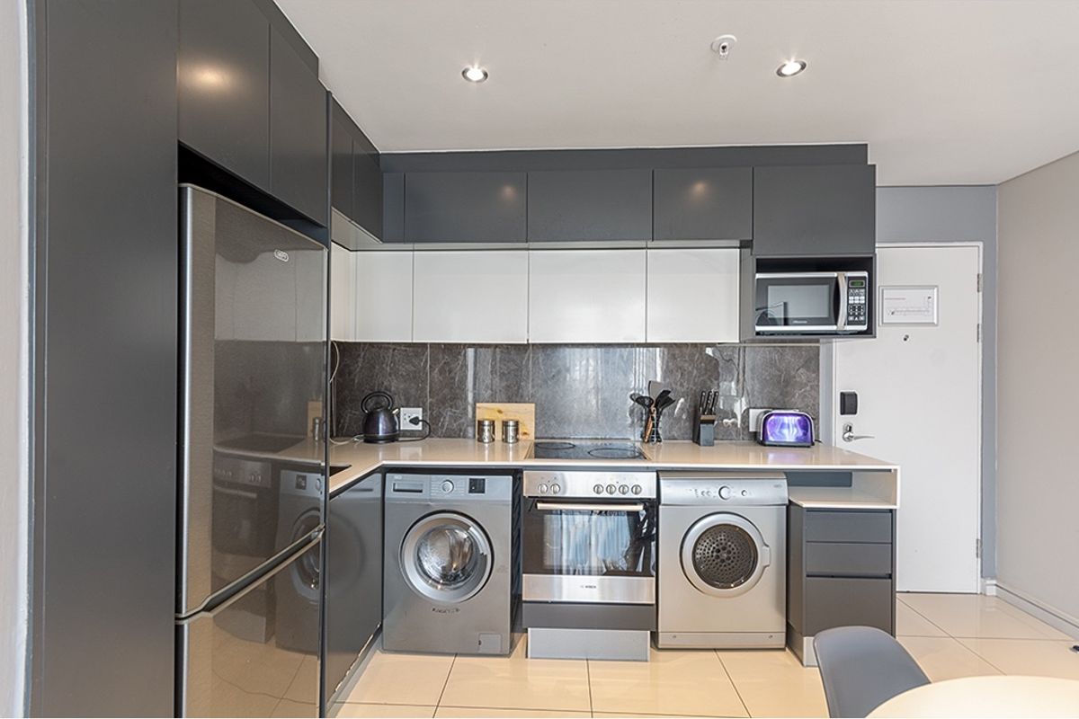 Modern kitchen featuring sleek two-tone cabinetry, stone countertops, integrated appliances, and high-quality tiled flooring in a contemporary apartment setting.