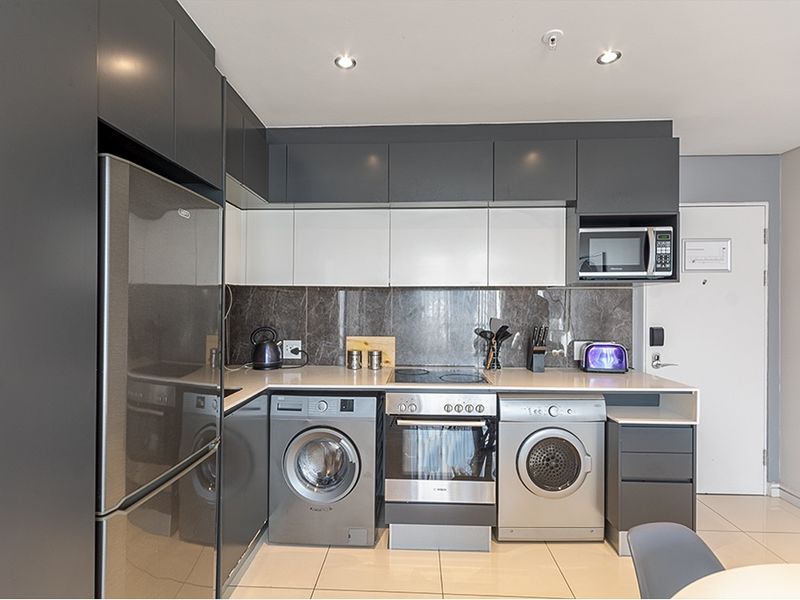 Modern kitchen featuring sleek two-tone cabinetry, stone countertops, integrated appliances, and high-quality tiled flooring in a contemporary apartment setting.