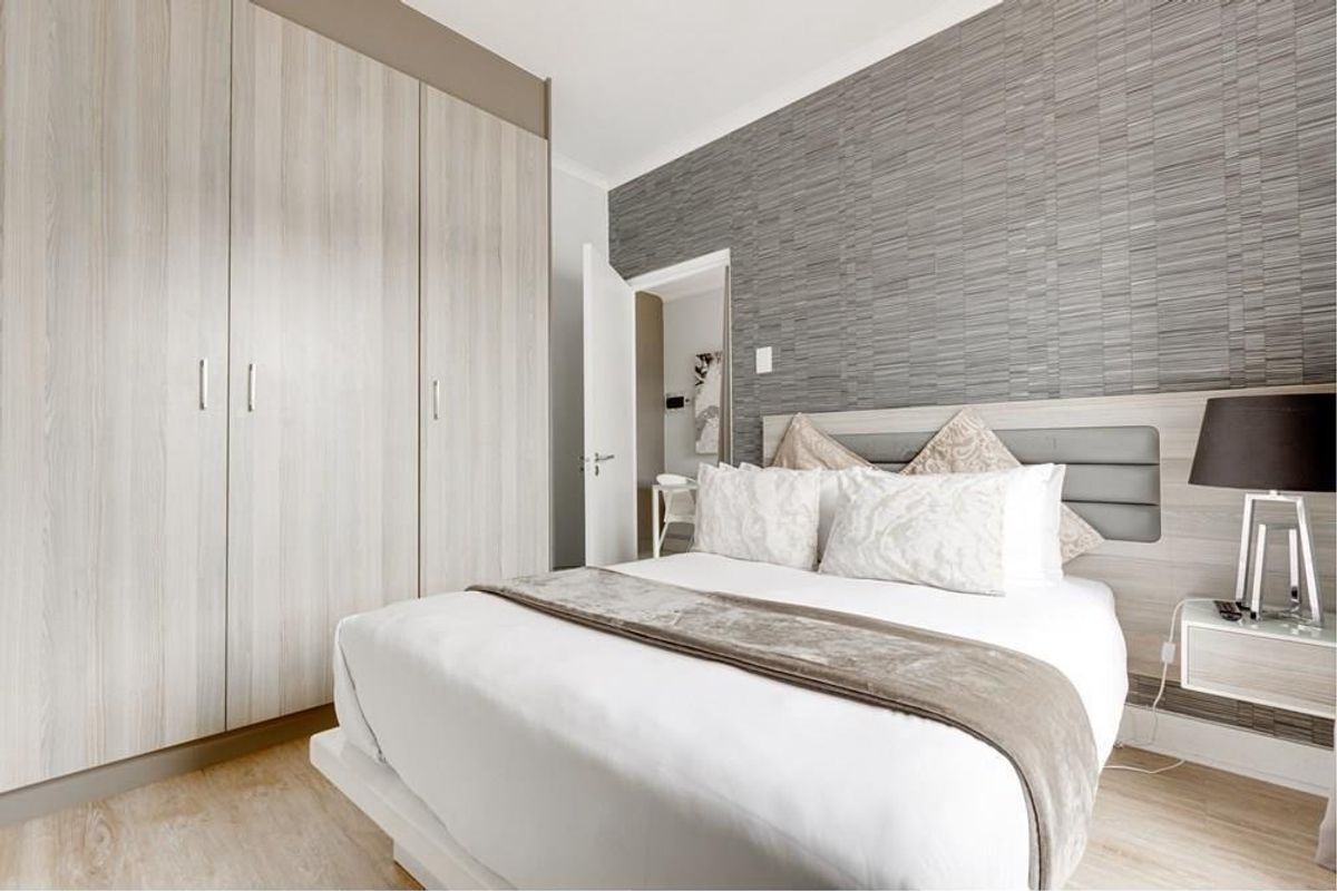 A well-maintained bedroom featuring light wood-grain built-in wardrobes, modern laminate flooring, and a stylish textured feature wall behind the bed.
