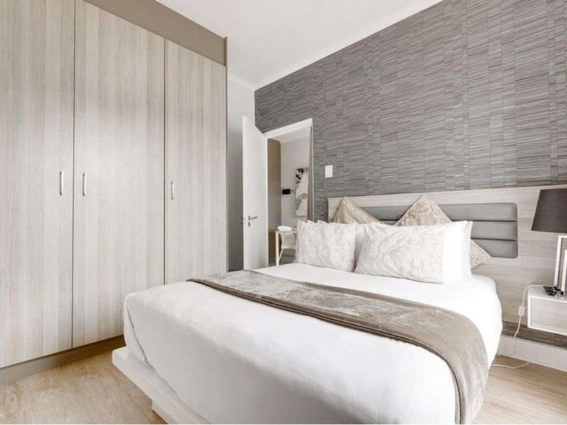 A well-maintained bedroom featuring light wood-grain built-in wardrobes, modern laminate flooring, and a stylish textured feature wall behind the bed.