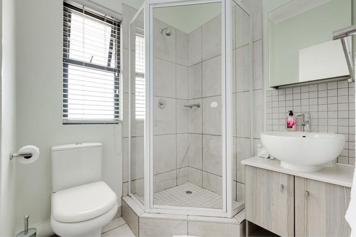 A clean, functional bathroom featuring a corner shower enclosure, a modern vessel sink on a vanity cabinet, and neutral wall tiling.
