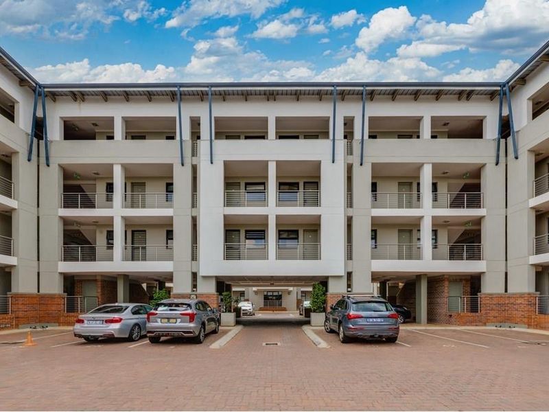 Front elevation of a modern multi-story apartment complex featuring paved parking areas and structured architectural design.