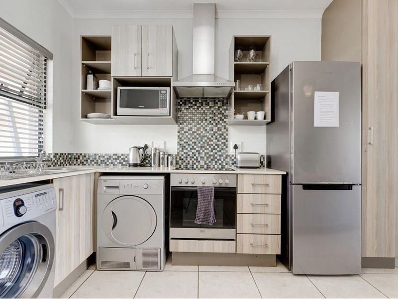 Compact modern kitchen featuring light wood-grain cabinetry, mosaic tile backsplash, integrated stainless steel appliances, and tiled flooring.