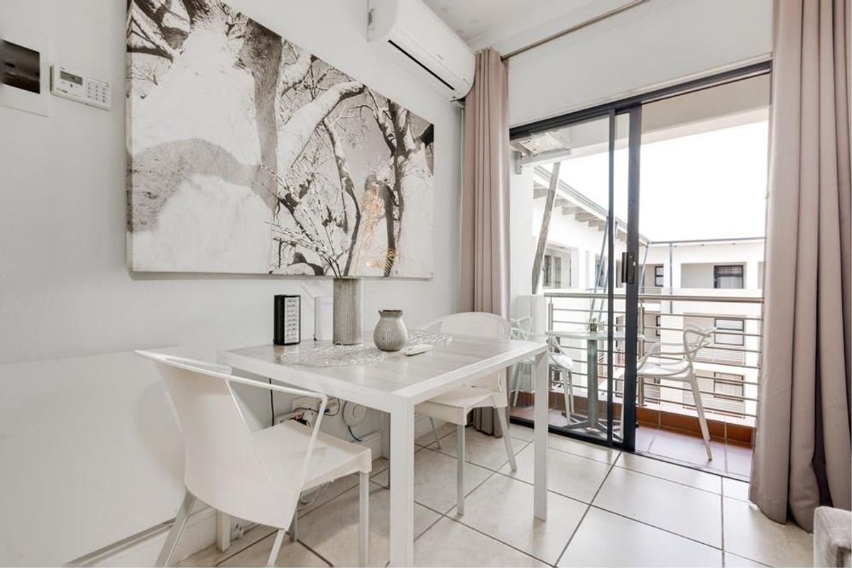 A bright living area featuring tiled flooring, a wall-mounted air conditioning unit, and direct access to a private balcony through sliding glass doors.