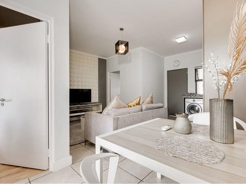 An open-plan living and dining area featuring tiled and laminate flooring, a textured feature wall, and a dedicated laundry nook with appliance connections.