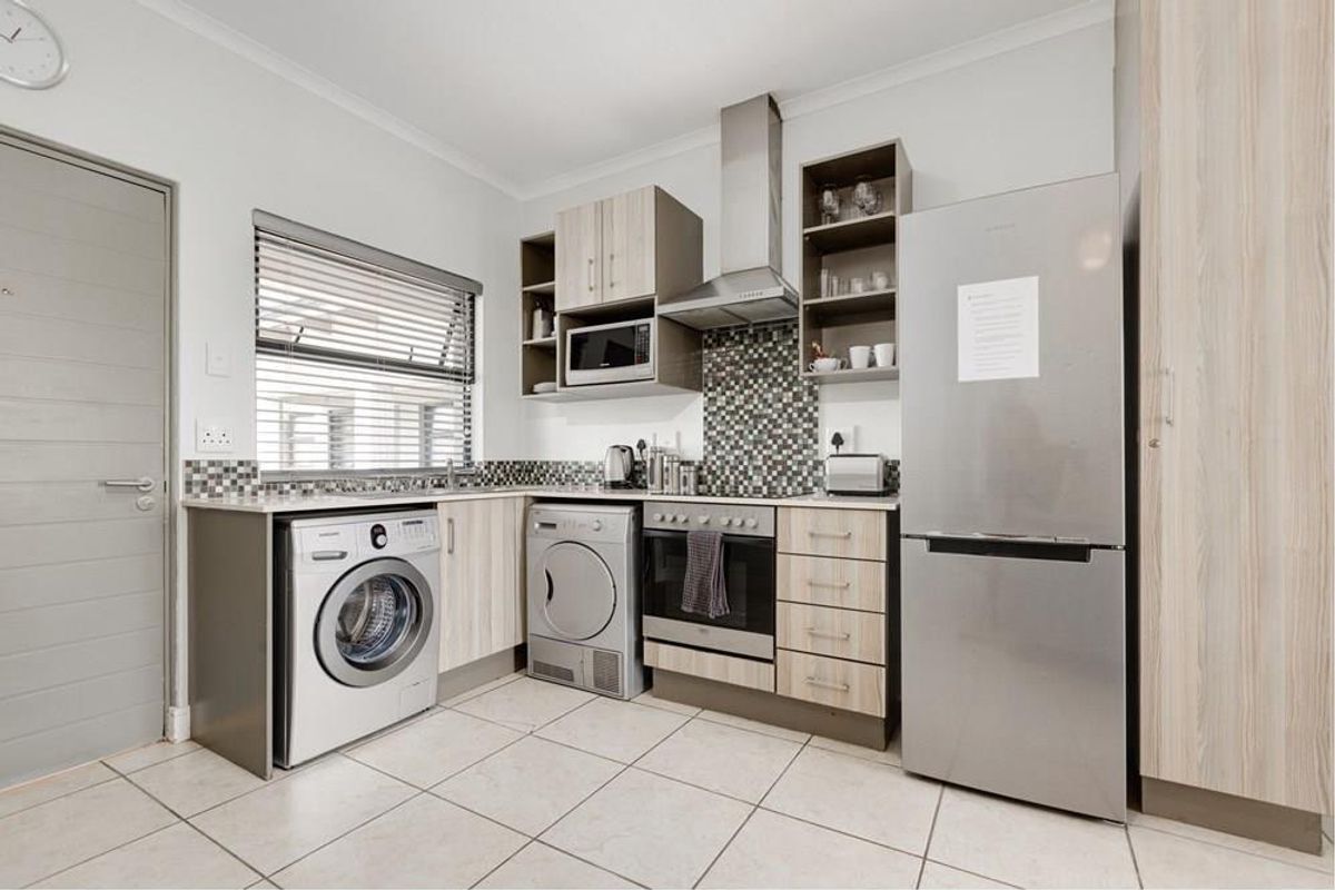 Modern kitchen featuring light wood-finish cabinetry, mosaic tile backsplash, integrated appliances, and tiled flooring with a functional layout.