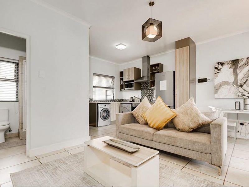 An open-plan living area featuring a modern kitchen with built-in cabinetry, tiled floors, and an adjacent bathroom with a toilet.