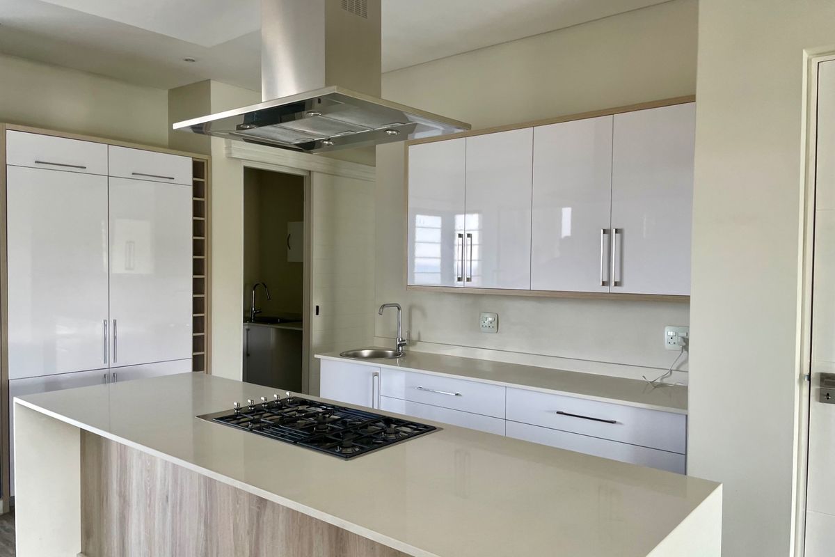 Modern kitchen featuring a central island with a gas hob, sleek white cabinetry, stone countertops, and a stainless steel extractor fan.