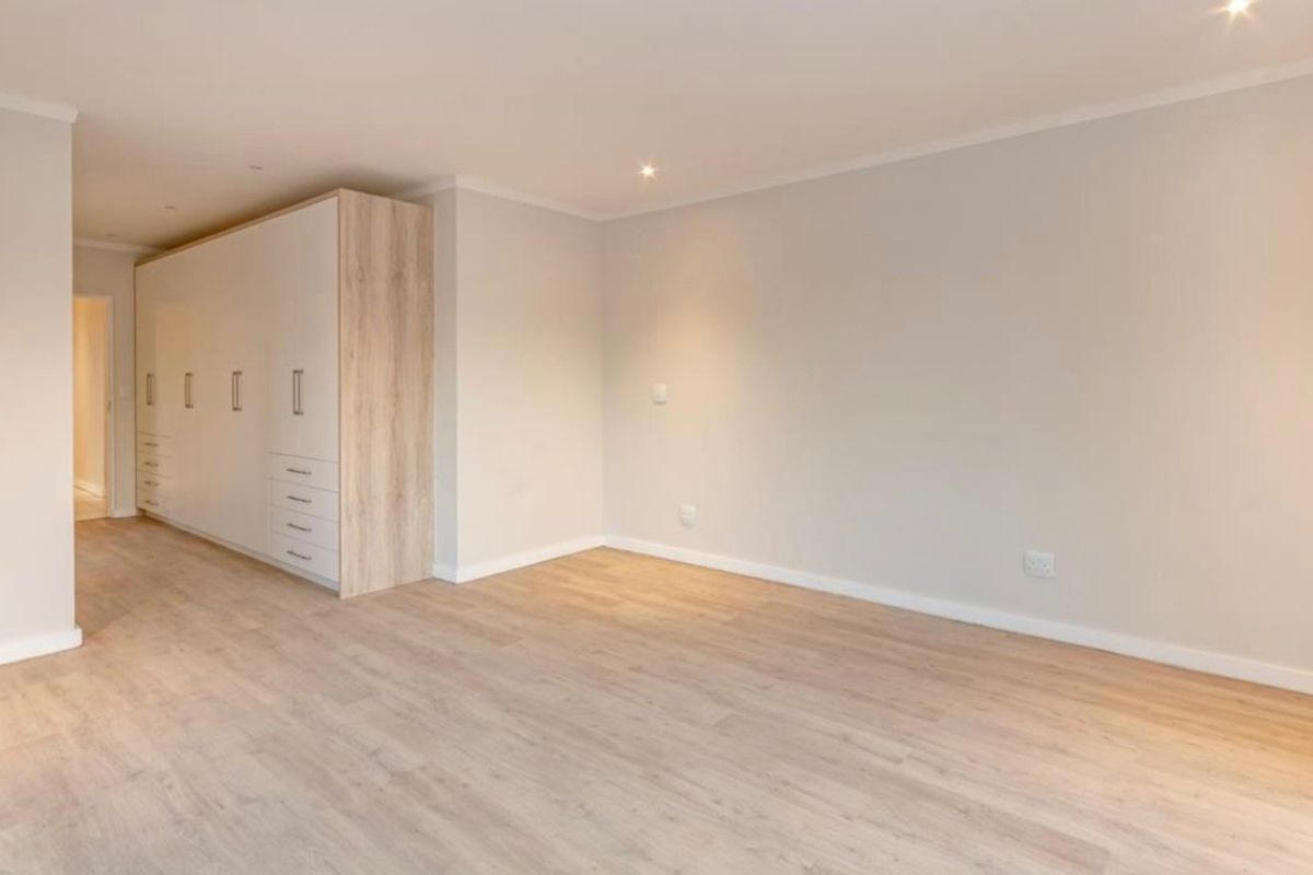 A bright, modern bedroom featuring light-toned laminate flooring and extensive built-in cabinetry with a clean, neutral aesthetic.