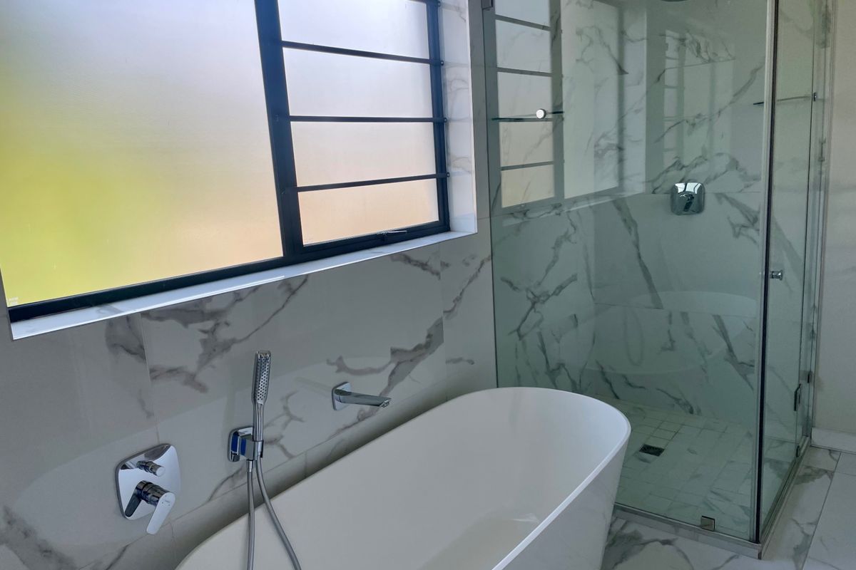 Modern bathroom featuring a sleek freestanding bathtub, a glass-enclosed shower with rainfall fixture, and elegant marble-look tiling throughout.