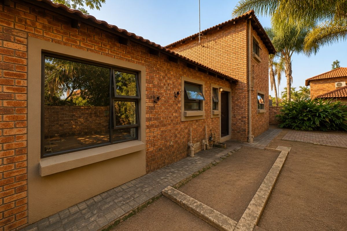 Rear view of a double-storey townhouse featuring face brick construction, tiled roofing, and paved outdoor pathways.