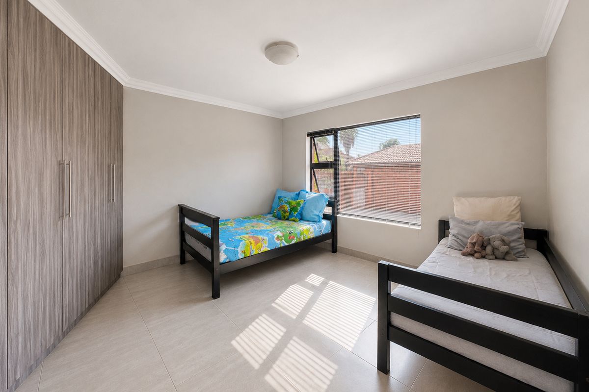 A well-maintained bedroom featuring neutral tiled flooring, built-in cupboards with a wood-grain finish, and an aluminium-framed window.