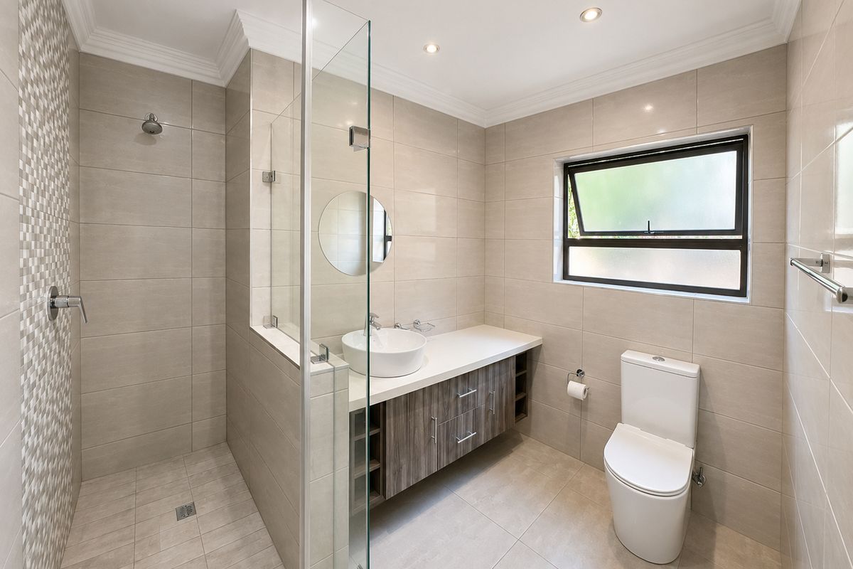 Modern bathroom featuring a walk-in shower with glass screen, contemporary vanity with countertop basin, neutral floor-to-ceiling tiling, and a toilet.