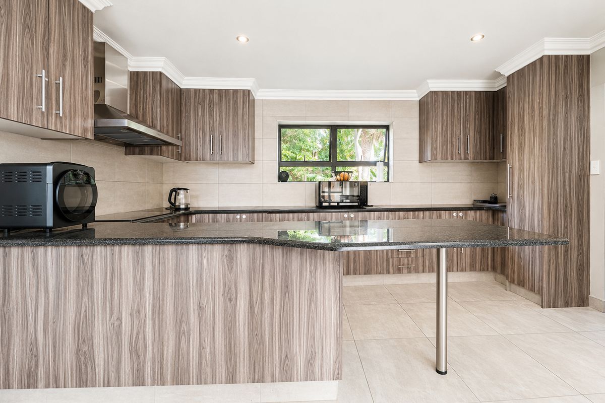 Modern kitchen featuring wood-grain laminate cabinetry, granite countertops, a breakfast bar, and neutral tiled flooring with a clean, functional layout.