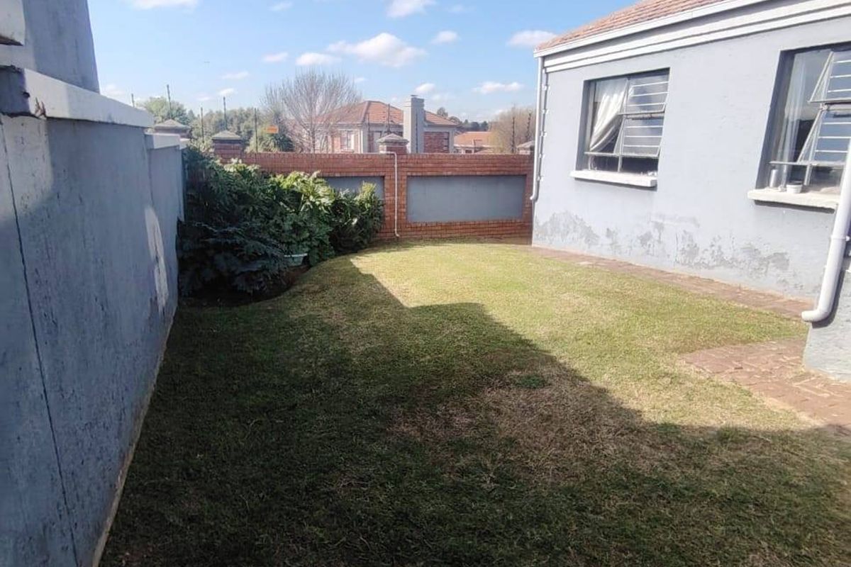 Rear garden area featuring a lawn, brick boundary wall, and exterior wall with visible paint deterioration and signs of rising damp.
