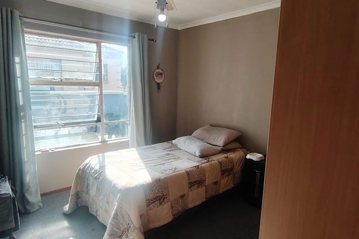 A functional bedroom featuring carpeted flooring, a ceiling fan, and a built-in cupboard, with natural light entering through an aluminium-framed window.