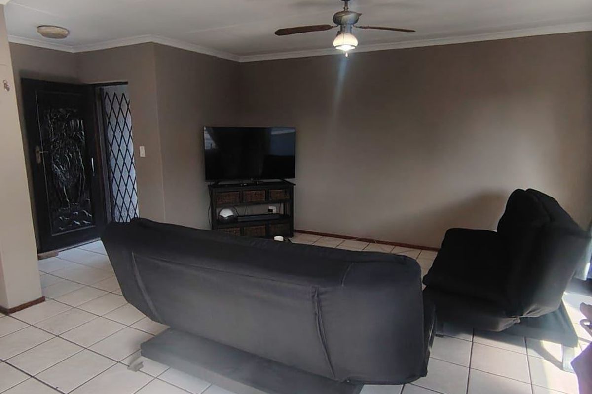 A living room featuring tiled flooring, a ceiling fan, and a security gate at the entrance.