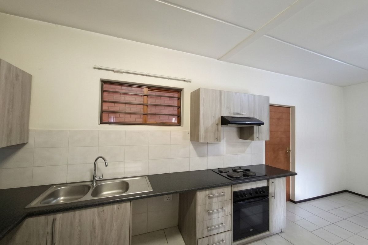 A clean, functional kitchen featuring light wood-finish cabinetry, dark laminate countertops, built-in oven and hob, and neutral tiled flooring.