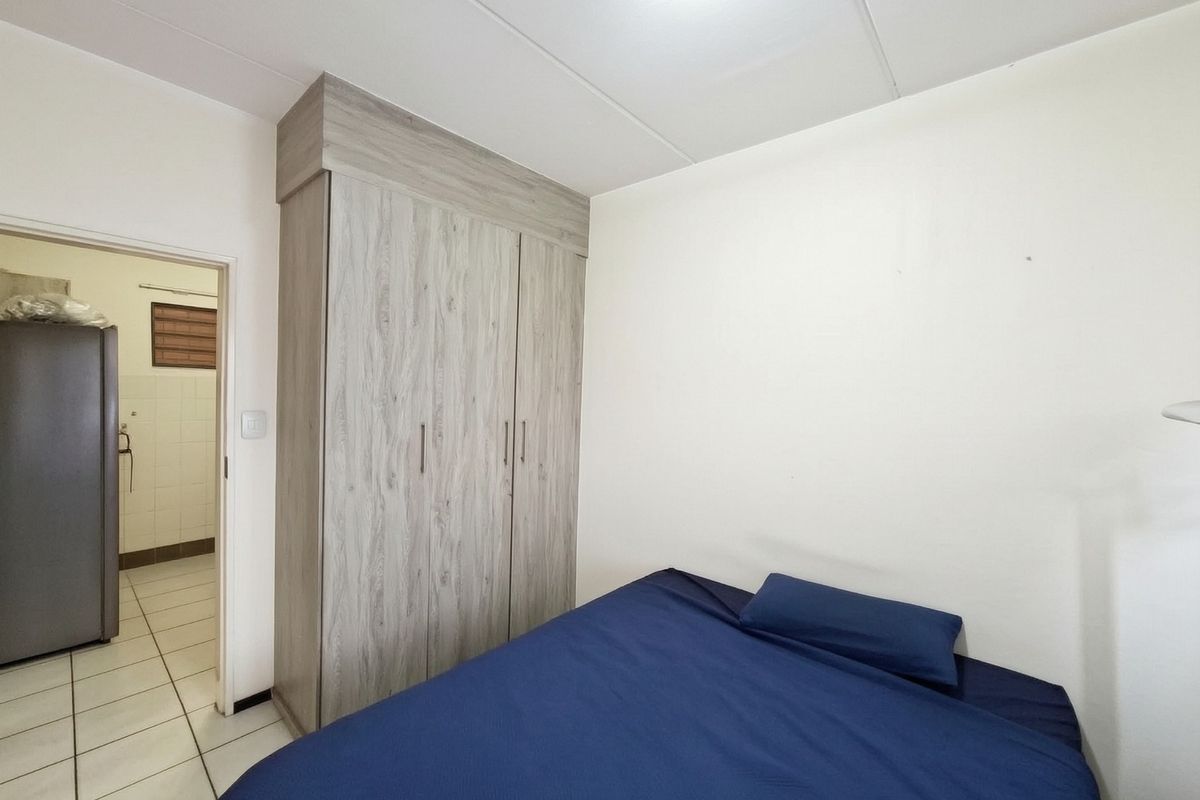 A bedroom featuring a built-in wood-look wardrobe and tiled flooring, with an adjacent view into a tiled utility or bathroom area.