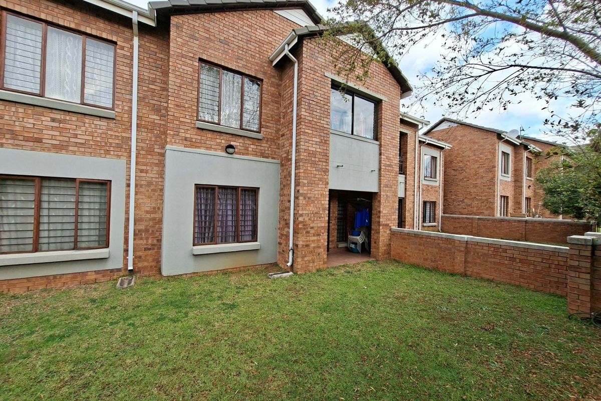 Rear view of a face brick apartment building featuring a private garden area, perimeter wall, and a covered patio space.