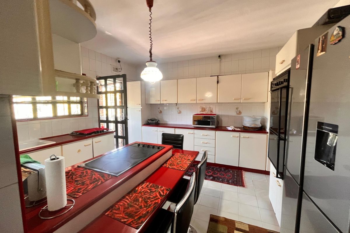 A functional kitchen featuring white cabinetry, red countertops, a built-in double oven, and an integrated electric cooktop with a breakfast bar.