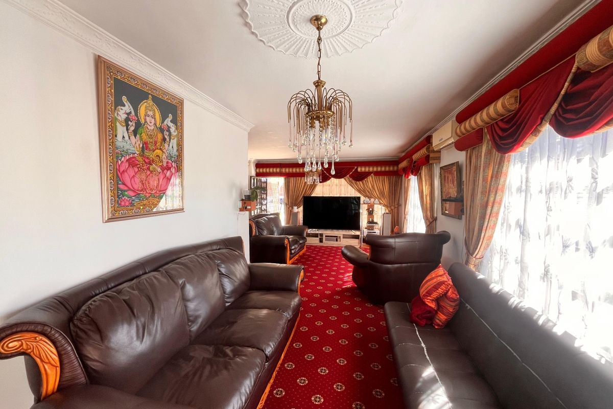 A traditional living room featuring a decorative ceiling rose, crystal chandelier, and coving, with a wall-mounted air conditioning unit.