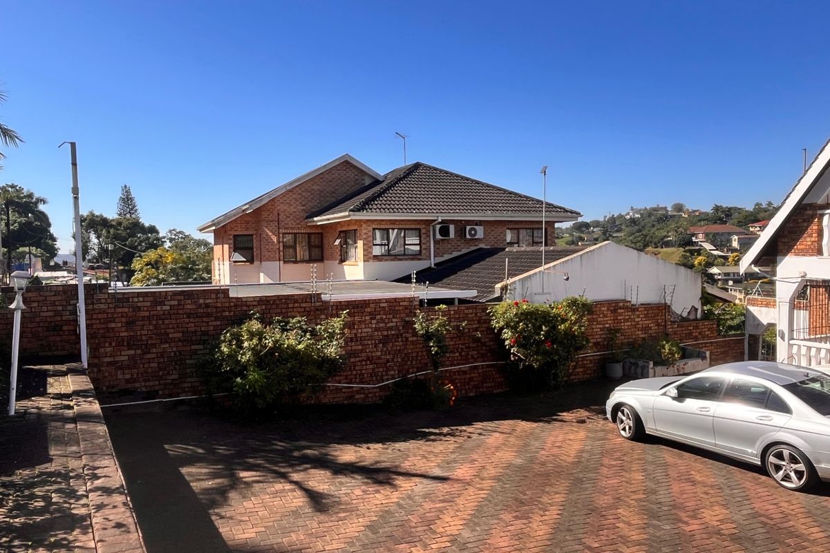 Rear view of the property featuring a brick boundary wall with electric fencing, paved driveway, and a multi-pitched tiled roof.