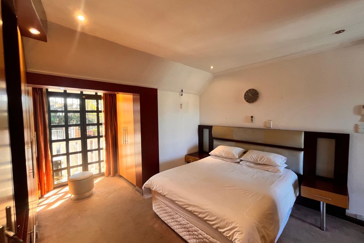 Spacious bedroom featuring built-in cupboards, sloped ceilings, recessed lighting, and a glass door providing access to an outdoor area.