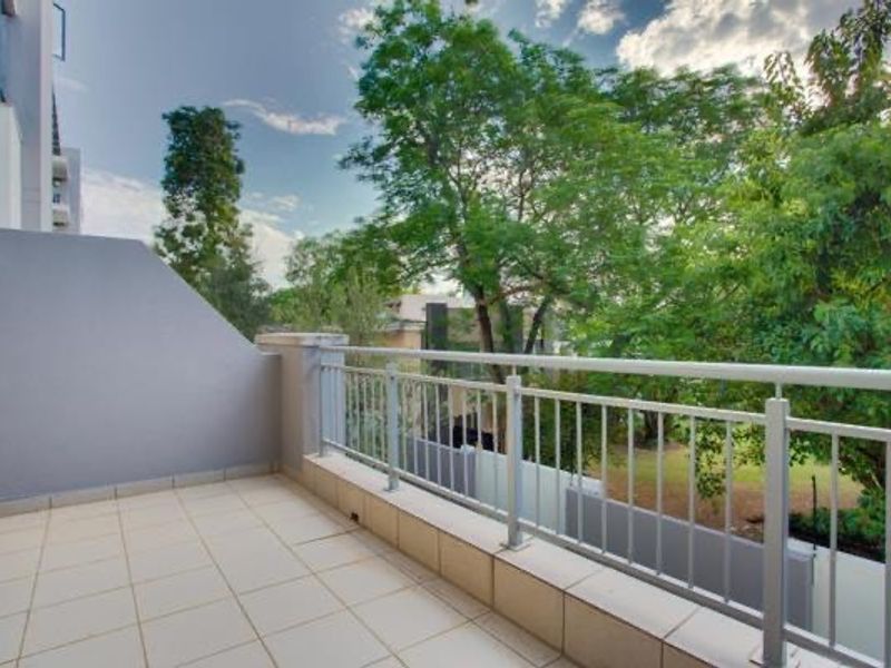 A clean, tiled balcony featuring a metal balustrade and pleasant views of surrounding trees, providing a private outdoor space.