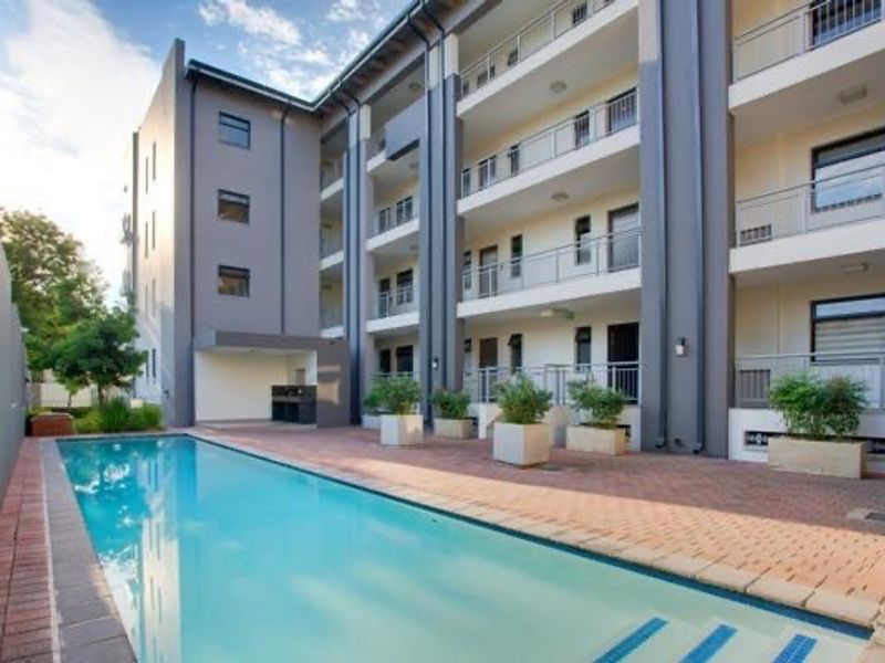 A well-maintained apartment complex pool area featuring a paved deck, built-in braai facilities, and multiple levels of balconies overlooking the swimming pool.