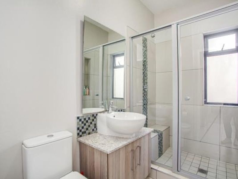 Modern bathroom featuring a vessel sink on a wood-finish vanity, a glass-enclosed shower with mosaic tile accents, and a clean, neutral aesthetic.