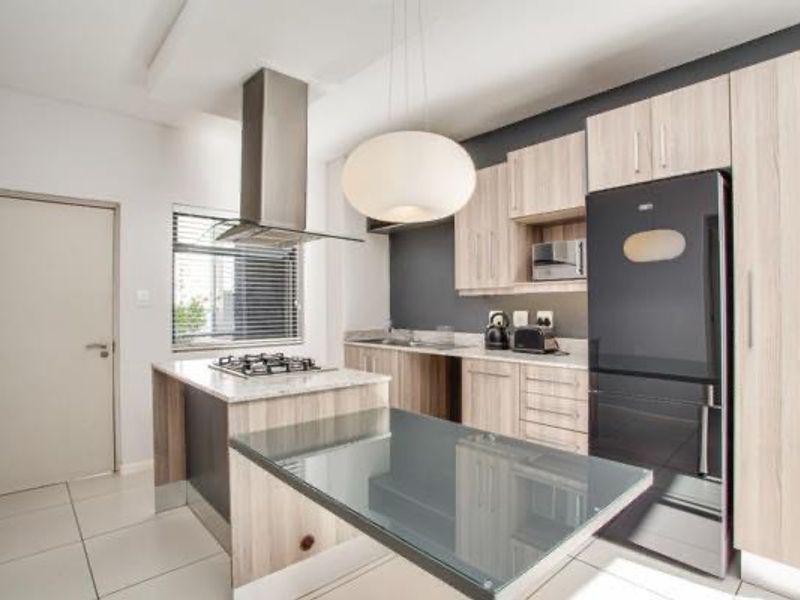 Modern kitchen featuring light wood cabinetry, stone countertops, a gas hob with stainless steel extractor, and integrated appliances in a clean, contemporary layout.
