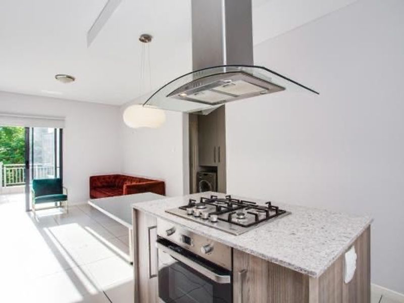 Modern open-plan living area featuring a kitchen island with a gas hob, built-in oven, extractor fan, and direct access to a balcony.