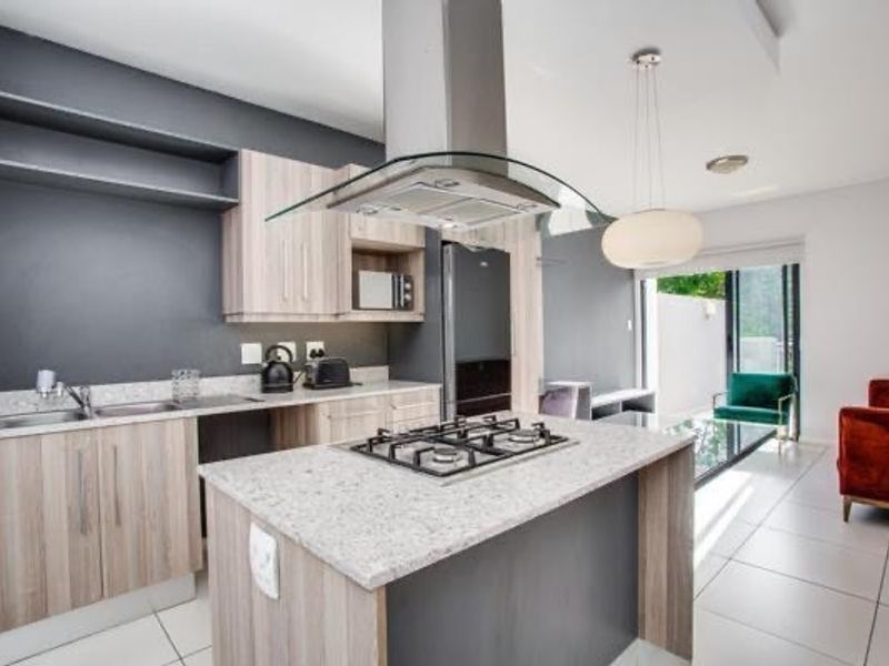 Modern open-plan kitchen featuring a central island with gas hob, stone countertops, and sleek cabinetry, seamlessly flowing into the living area.