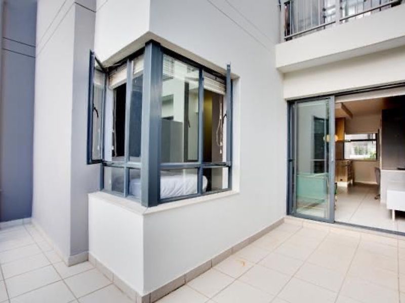 A clean, modern balcony featuring tiled flooring, a corner window, and sliding glass doors providing access to the interior living space.