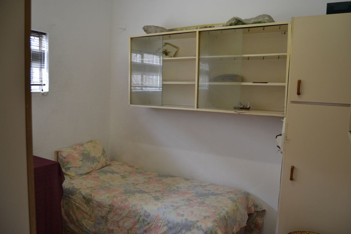 A compact bedroom featuring built-in cabinetry and wall-mounted storage units, offering functional space with dated finishes in need of modernization.