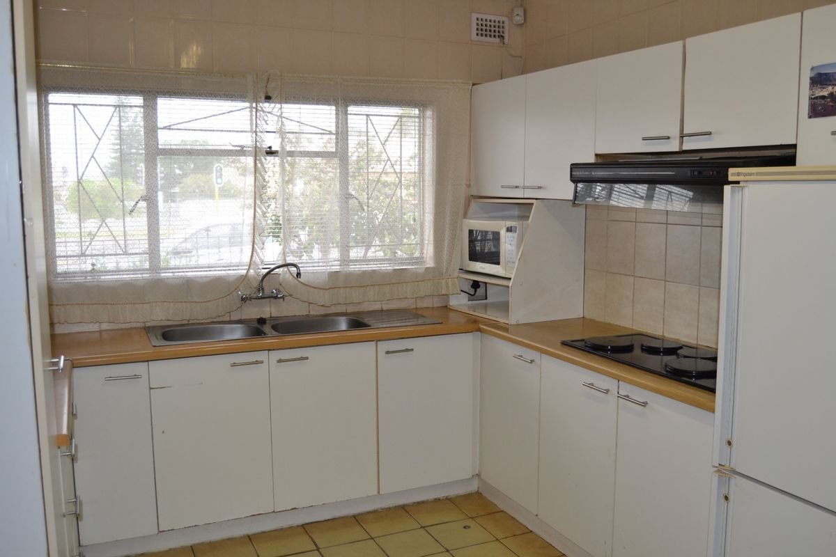 A functional kitchen featuring white cabinetry, laminate countertops, a double sink, and an integrated electric hob with an extractor fan.
