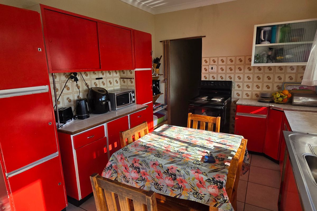 A functional kitchen featuring vibrant red cabinetry, tiled backsplash, and a stainless steel sink, offering a dated aesthetic with potential for modernization.