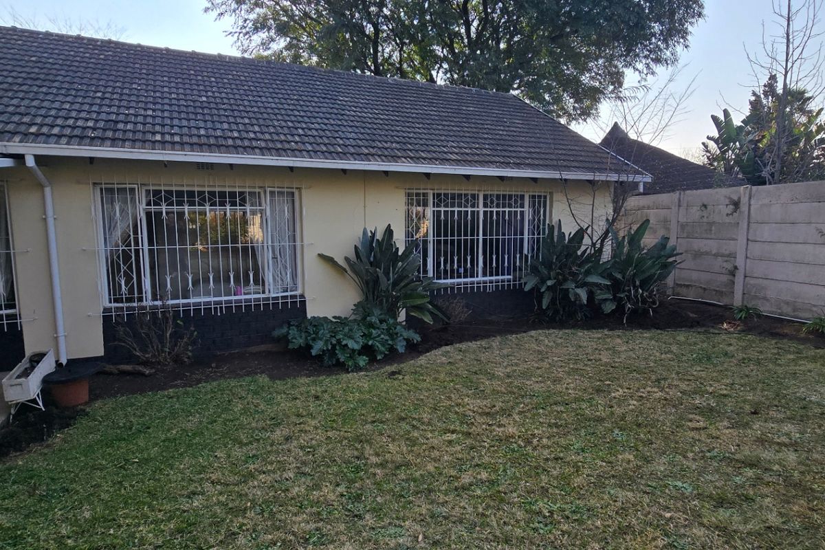 Rear view of the house featuring a tiled roof, security bars on windows, a paved patio area, and a private garden with perimeter walling.